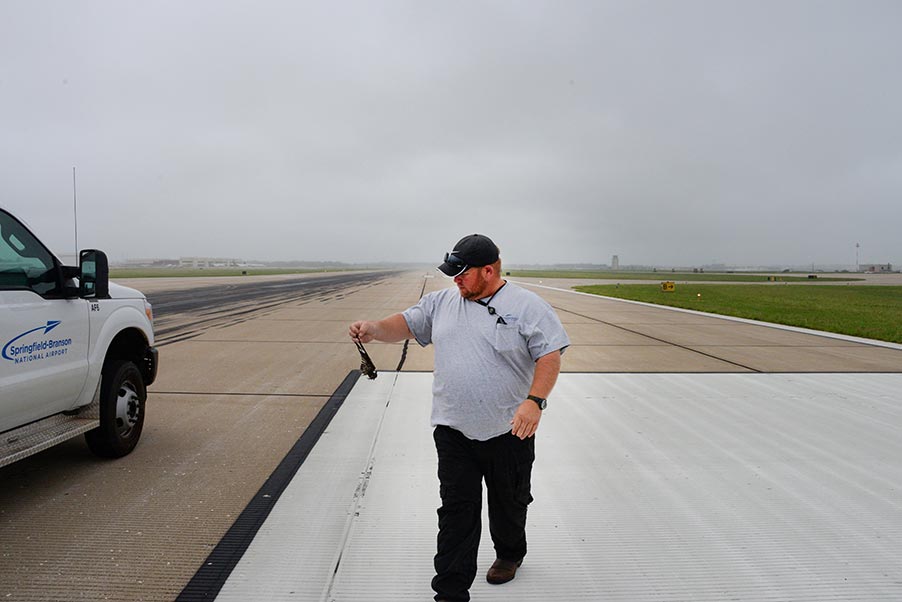 Image; An airport maintenance supervisor collects a dead bird during a runway inspection